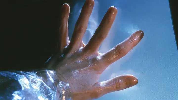 Y2K high fashion editorial, a 2001 couture magazine story: a close-up of a pale freckled palm and fingertips pressed flat against the inside of a glowing translucent CRT screen glass, seen from outside the screen in…