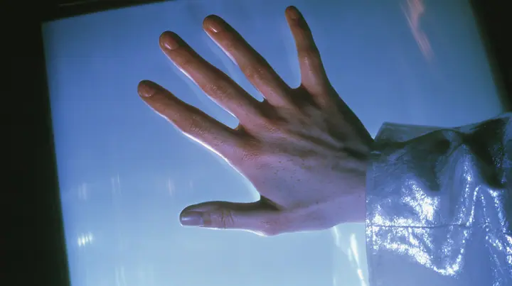 Y2K high fashion editorial, a 2001 couture magazine story: a close-up of a pale freckled palm and fingertips pressed flat against the inside of a glowing translucent CRT screen glass, seen from outside the screen in…