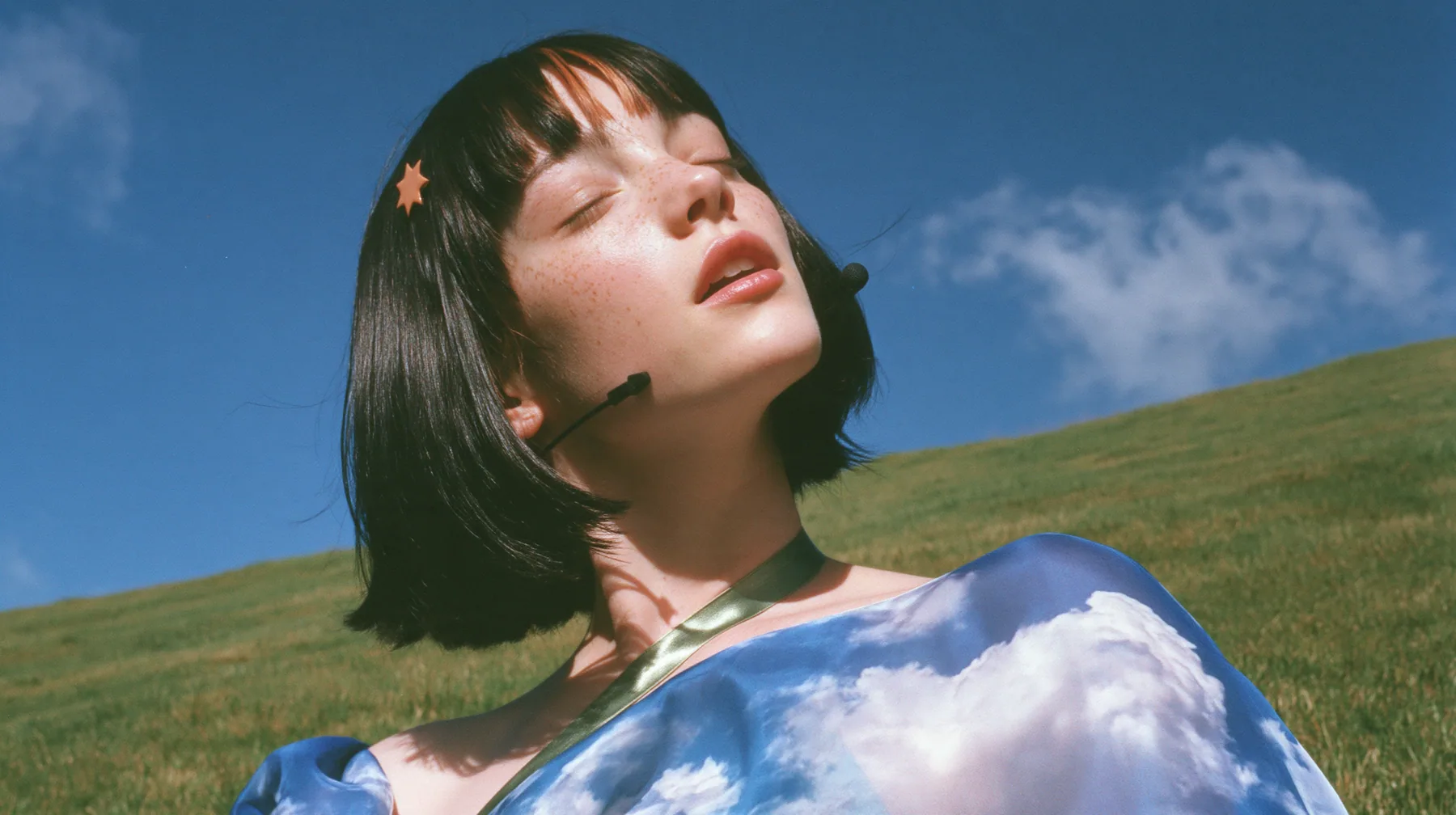 Y2K high fashion editorial, 2001: a medium shot of a Caucasian American woman in her mid-twenties with pale skin and light freckles, a glossy black blunt jaw-length bob with heavy straight bangs and one clay-orange…