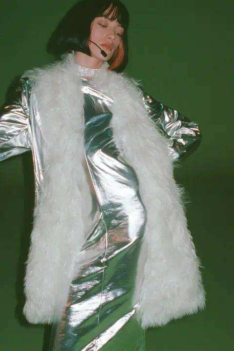 Y2K high fashion editorial, a 2001 couture magazine story: full-length shot, head to toe with the feet in frame, of a young Caucasian American woman with pale skin and a glossy black blunt bob with heavy straight…
