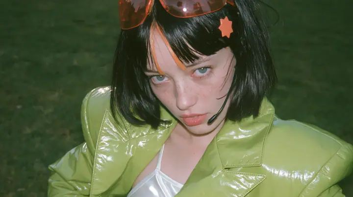Y2K high fashion editorial, a 2001 couture magazine story: a medium shot of a Caucasian American woman in her mid-twenties with pale skin and light freckles, a glossy black blunt jaw-length bob with heavy straight…