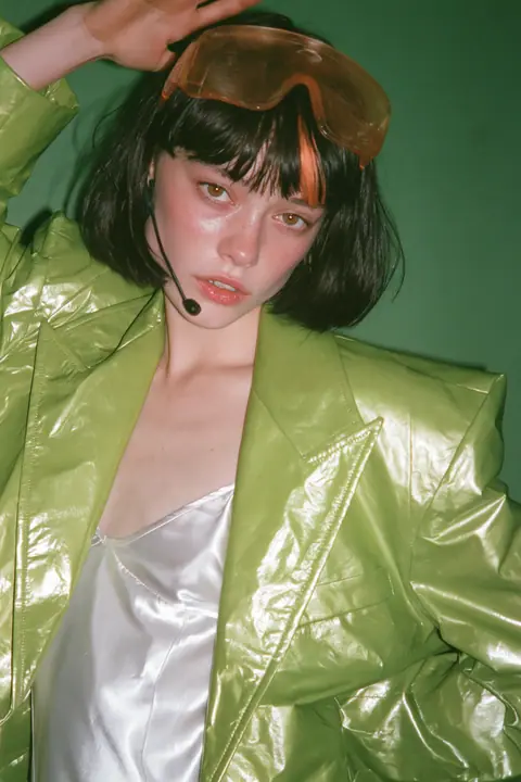 Y2K high fashion editorial, a 2001 couture magazine story: full-length shot, head to toe with the feet in frame, of a young Caucasian American woman with pale skin and a glossy black blunt bob with heavy straight…