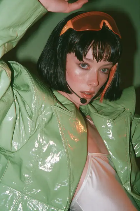 Y2K high fashion editorial, a 2001 couture magazine story: full-length shot, head to toe with the feet in frame, of a young Caucasian American woman with pale skin and a glossy black blunt bob with heavy straight…