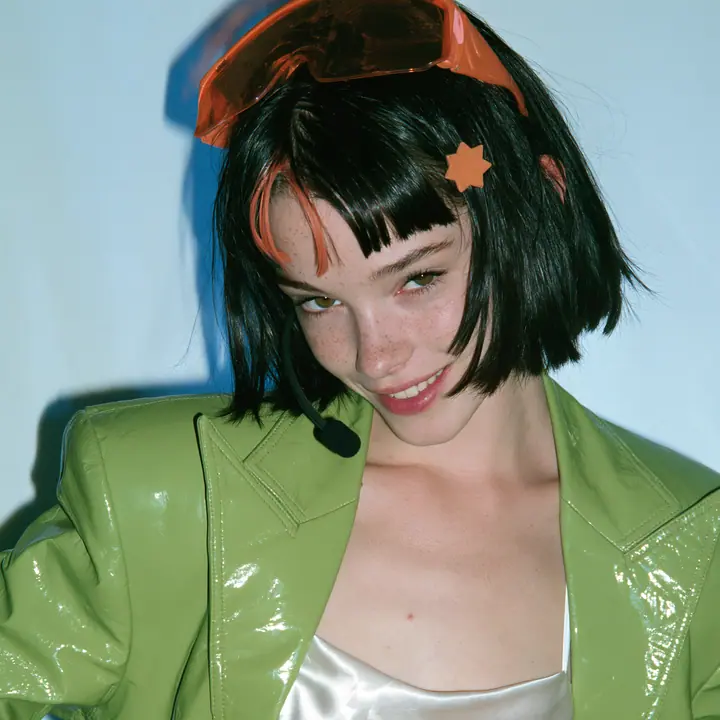 Y2K high fashion editorial, a 2001 couture magazine story: a square beauty portrait of a Caucasian American woman in her mid-twenties with pale skin and light freckles, a glossy black blunt jaw-length bob with heavy…