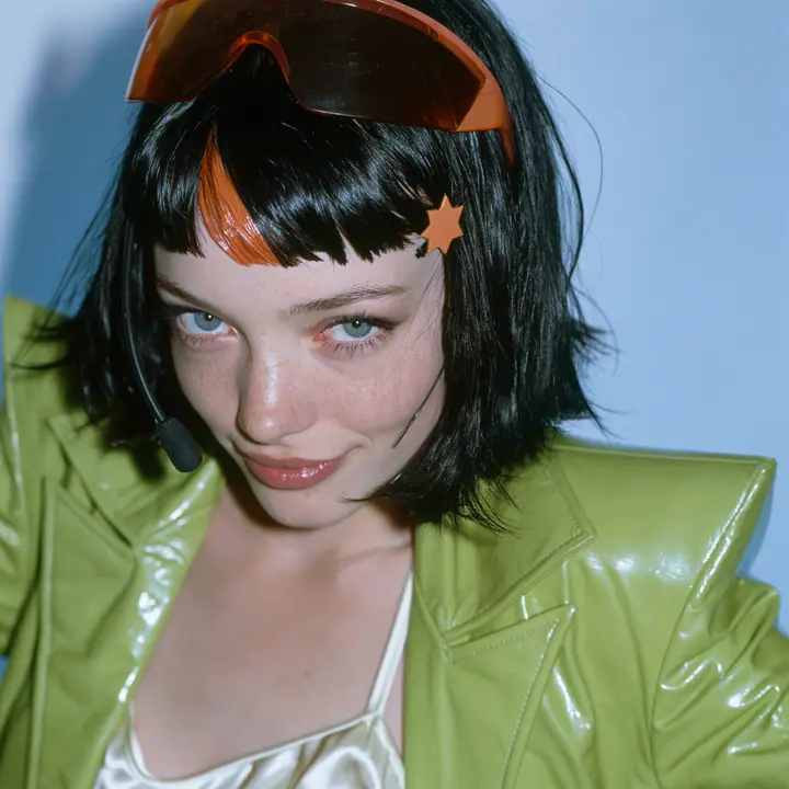 Y2K high fashion editorial, a 2001 couture magazine story: a square beauty portrait of a Caucasian American woman in her mid-twenties with pale skin and light freckles, a glossy black blunt jaw-length bob with heavy…