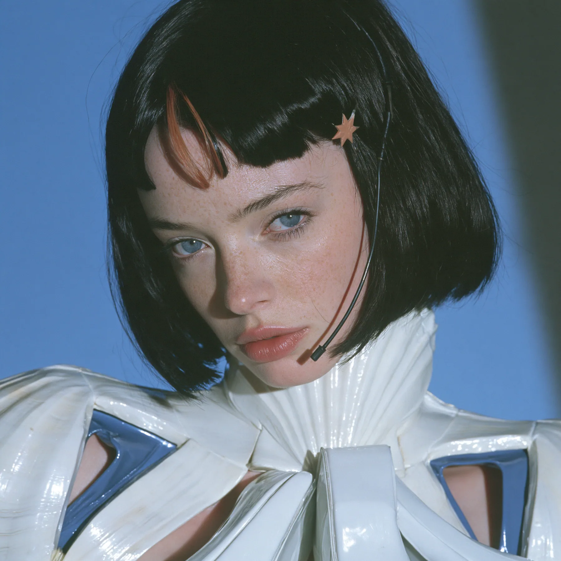 Y2K high fashion editorial, a 2001 couture magazine story: a square beauty portrait of a Caucasian American woman in her mid-twenties with pale skin and light freckles, a glossy black blunt jaw-length bob with heavy…