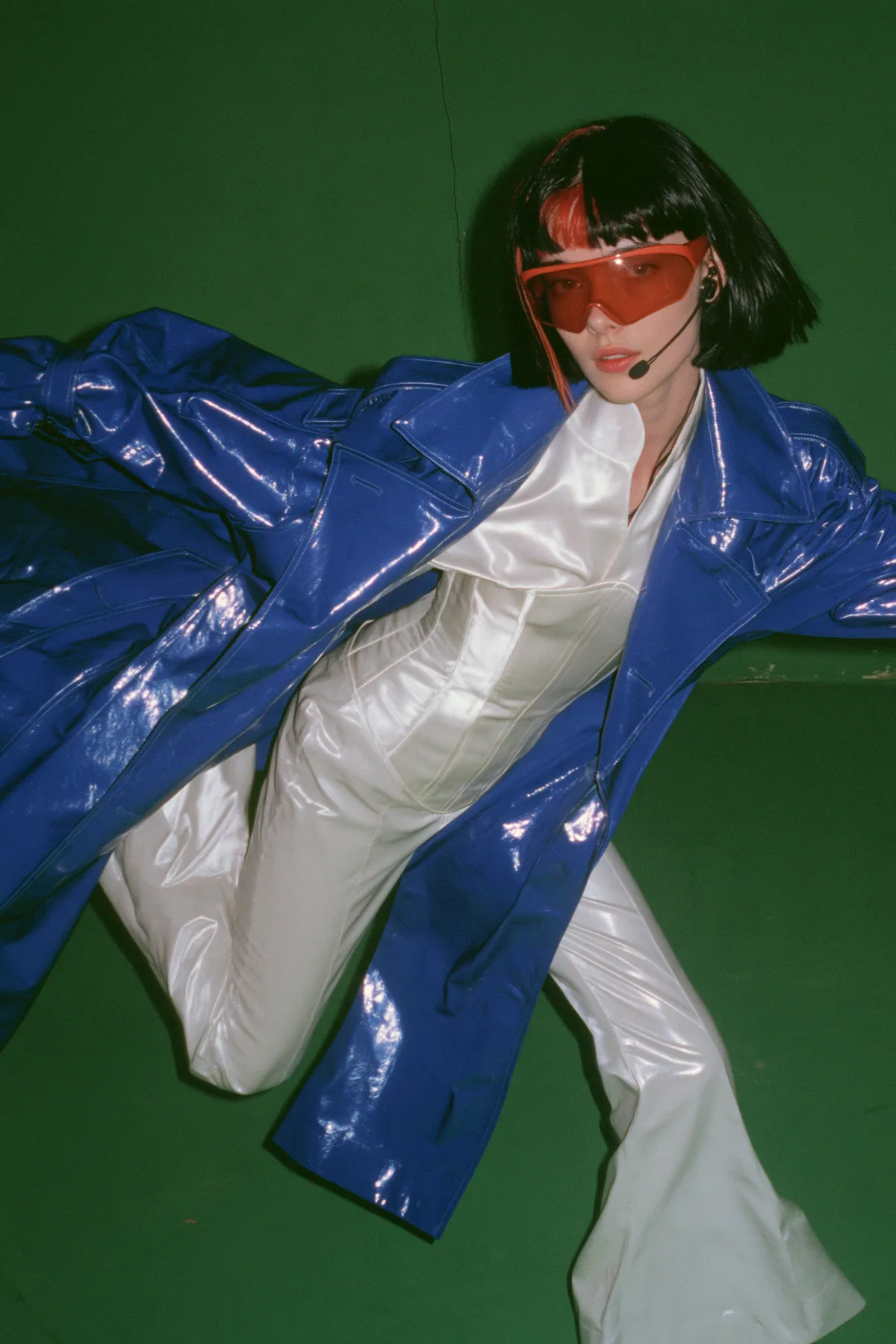 Y2K high fashion editorial, a 2001 couture magazine story: full-length shot of a young Caucasian American woman with pale skin and a glossy black blunt bob with heavy straight bangs and one clay-orange streak, a thin…