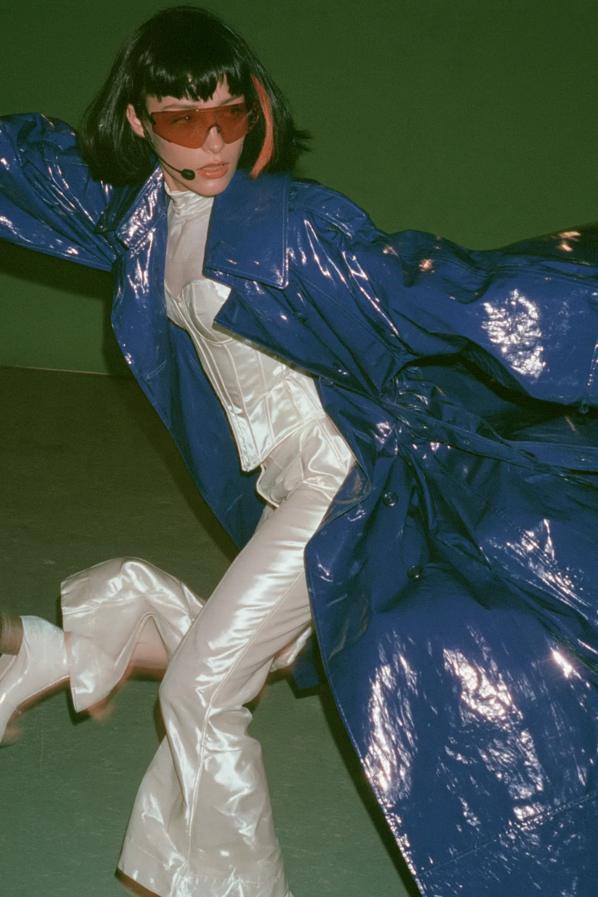 Y2K high fashion editorial, a 2001 couture magazine story: full-length shot of a young Caucasian American woman with pale skin and a glossy black blunt bob with heavy straight bangs and one clay-orange streak, a thin…