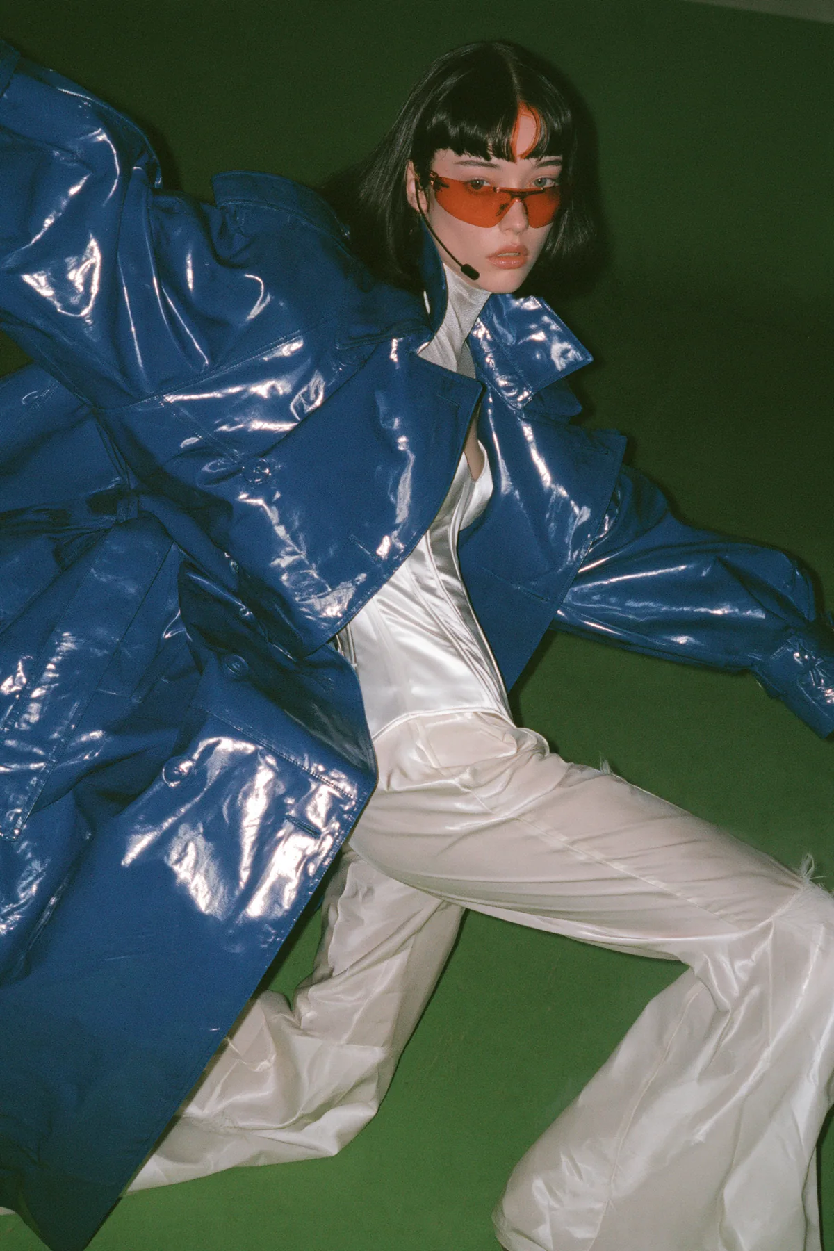 Y2K high fashion editorial, a 2001 couture magazine story: full-length shot of a young Caucasian American woman with pale skin and a glossy black blunt bob with heavy straight bangs and one clay-orange streak, a thin…