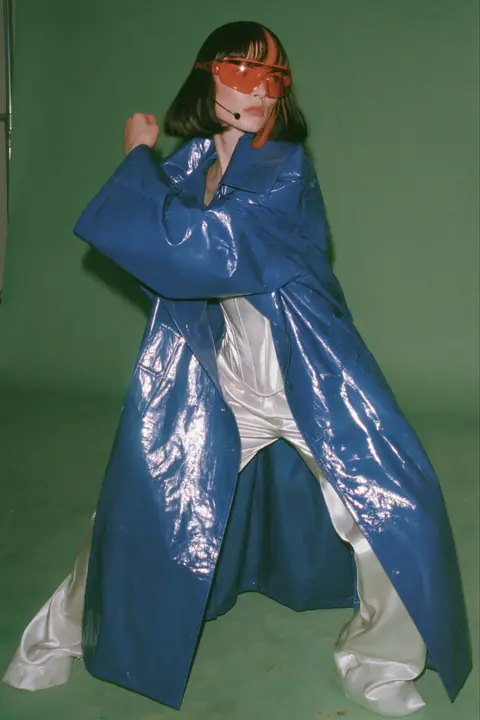 Y2K high fashion editorial, a 2001 couture magazine story: full-length shot, head to toe with the feet in frame, of a young Caucasian American woman with pale skin and a glossy black blunt bob with heavy straight…