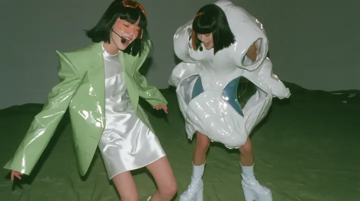 Y2K high fashion editorial, a 2001 couture magazine story: full-length shot of two identical women, both a young Caucasian American woman with pale skin and a glossy black blunt bob with heavy straight bangs and one…