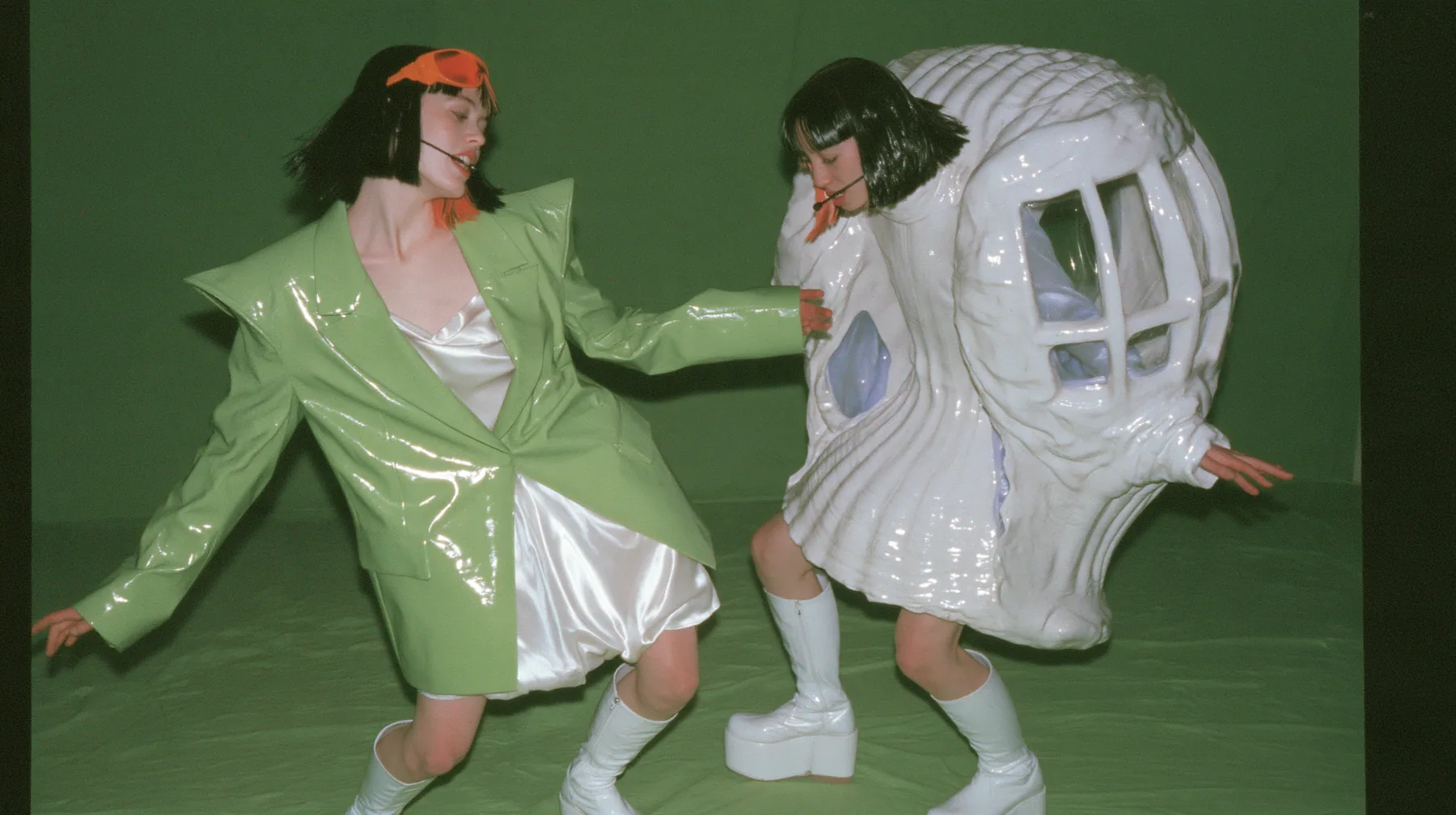 Y2K high fashion editorial, a 2001 couture magazine story: full-length shot of two identical women, both a young Caucasian American woman with pale skin and a glossy black blunt bob with heavy straight bangs and one…
