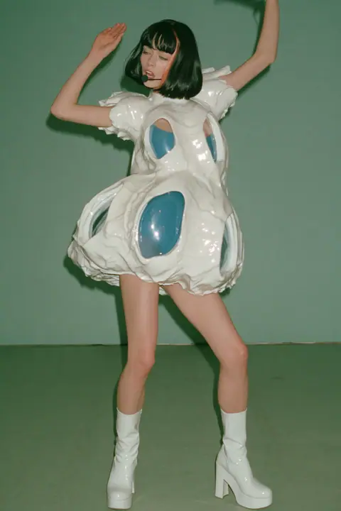 Y2K high fashion editorial, a 2001 couture magazine story: full-length shot, head to toe with the feet in frame, of a young Caucasian American woman with pale skin and a glossy black blunt bob with heavy straight…