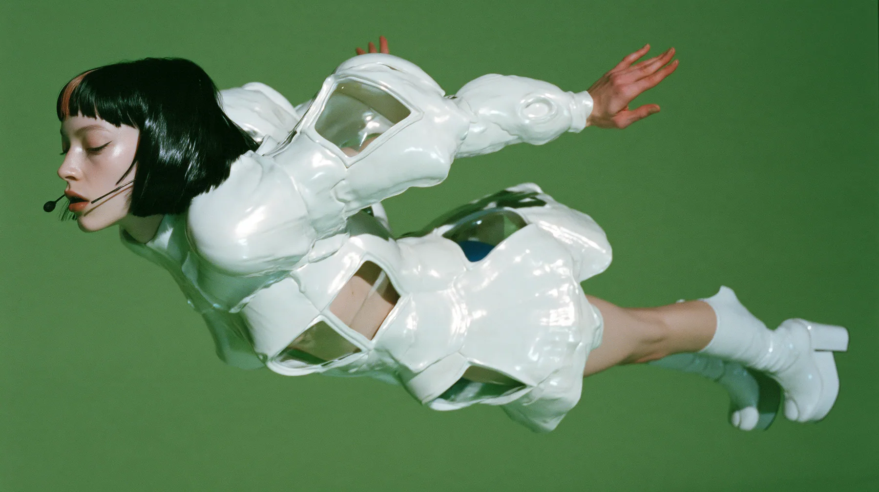 Y2K high fashion editorial, a 2001 couture magazine story: a full-length shot of a young Caucasian American woman with pale skin and a glossy black blunt bob with heavy straight bangs and one clay-orange streak, a…
