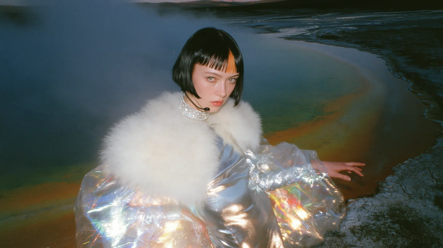 Y2K high fashion editorial, a 2001 couture magazine story: a wide shot of a young Caucasian American woman with pale skin and a glossy black blunt bob with heavy straight bangs and one clay-orange streak, a thin…