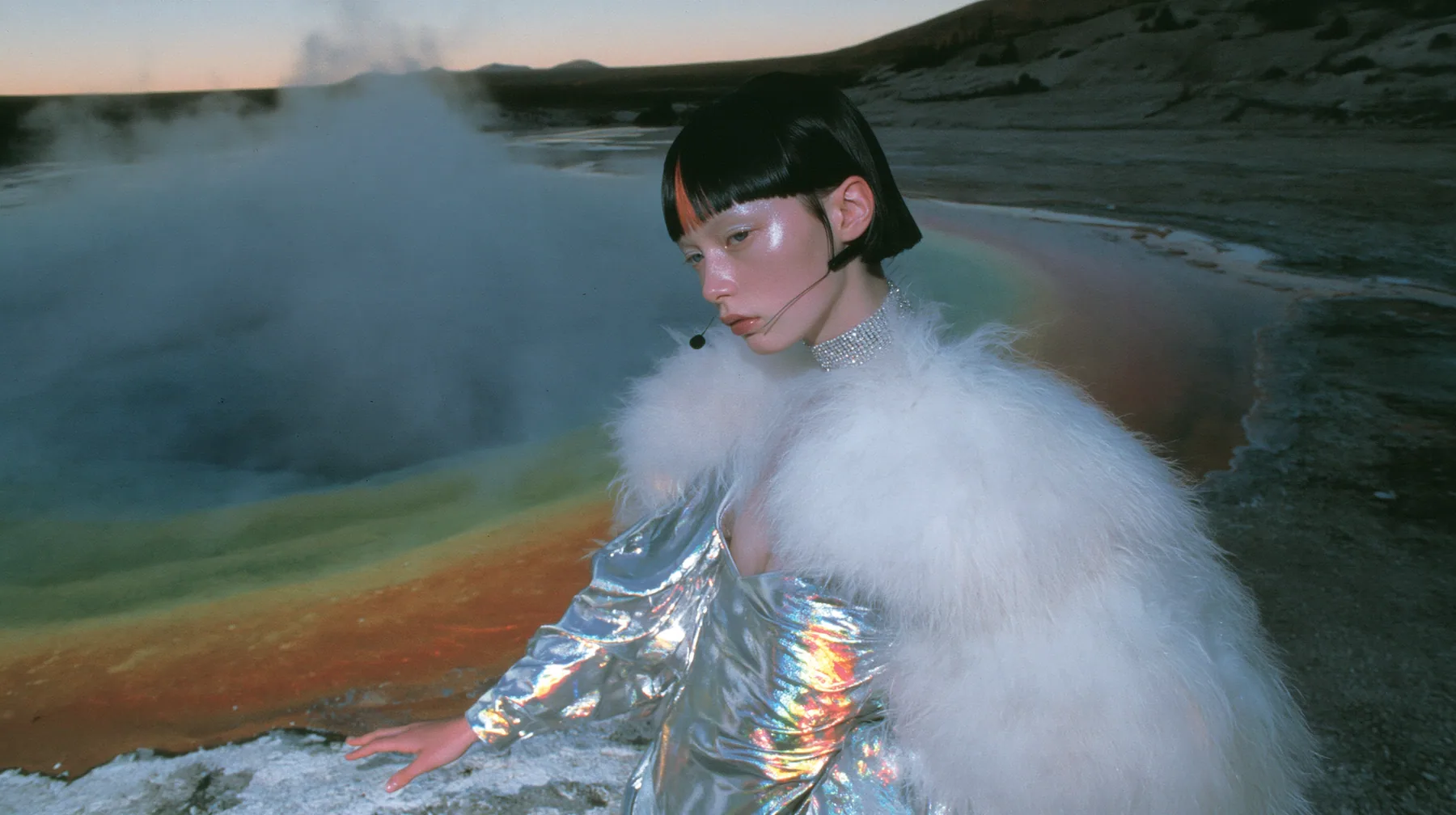 Y2K high fashion editorial, a 2001 couture magazine story: a wide shot of a young Caucasian American woman with pale skin and a glossy black blunt bob with heavy straight bangs and one clay-orange streak, a thin…