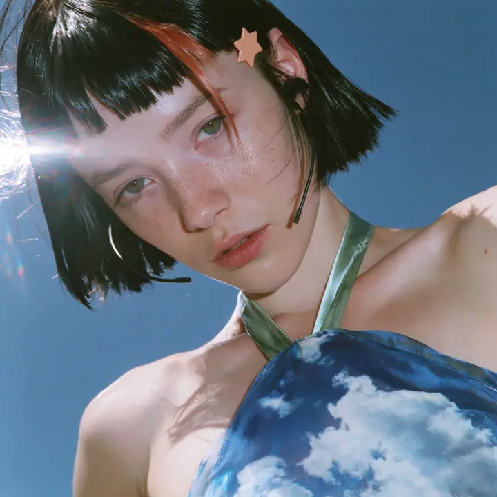 Y2K high fashion editorial, a 2001 couture magazine story: a square album cover photograph of a Caucasian American woman in her mid-twenties with pale skin and light freckles, a glossy black blunt jaw-length bob with…
