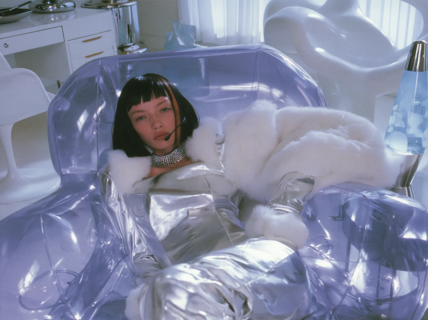 Y2K high fashion editorial, a 2001 couture magazine story: a young Caucasian American woman with pale skin and a glossy black blunt bob with heavy straight bangs and one clay-orange streak, a thin black headset…