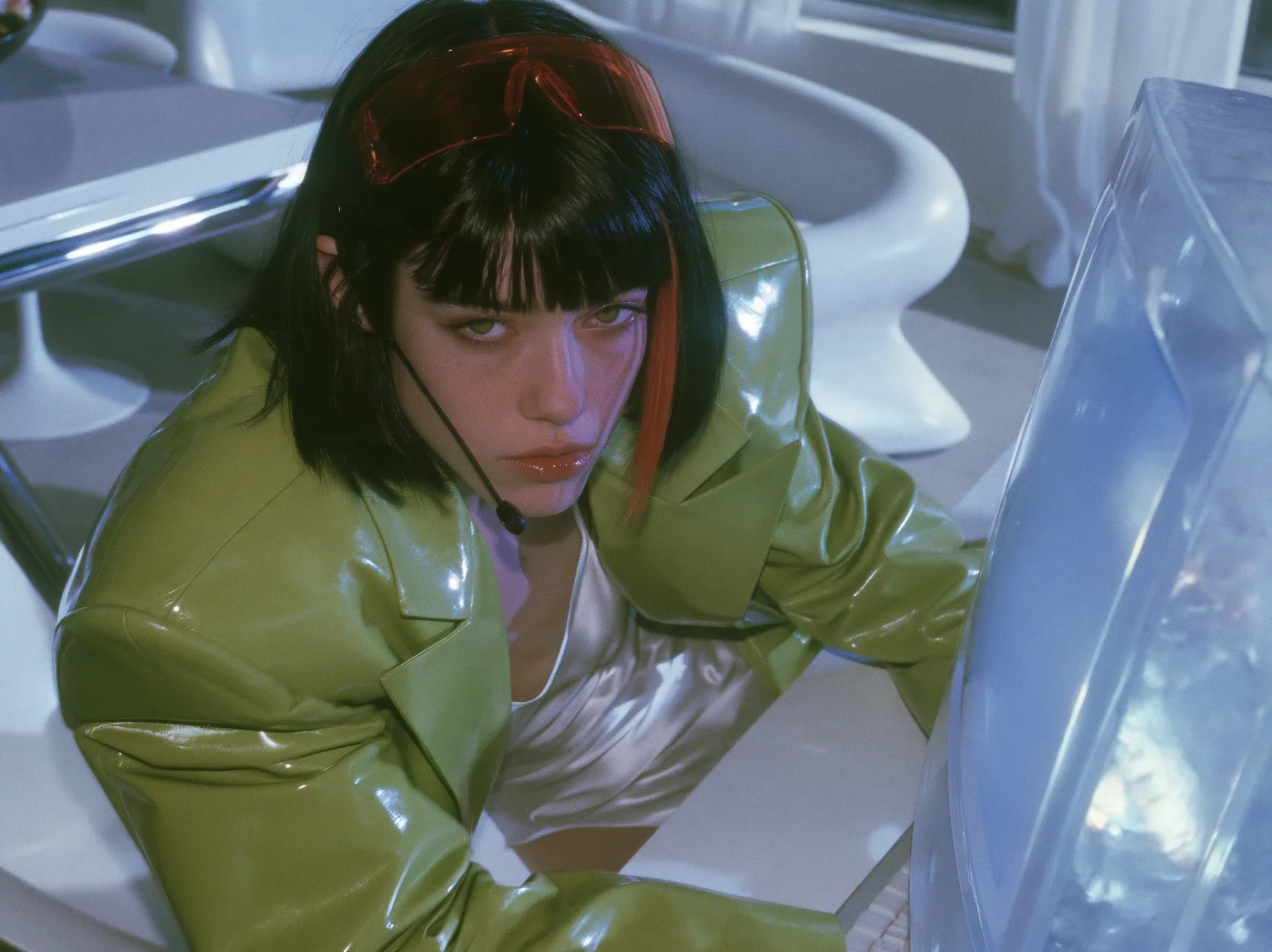 Y2K high fashion editorial, a 2001 couture magazine story: a young Caucasian American woman with pale skin and a glossy black blunt bob with heavy straight bangs and one clay-orange streak, a thin black headset…