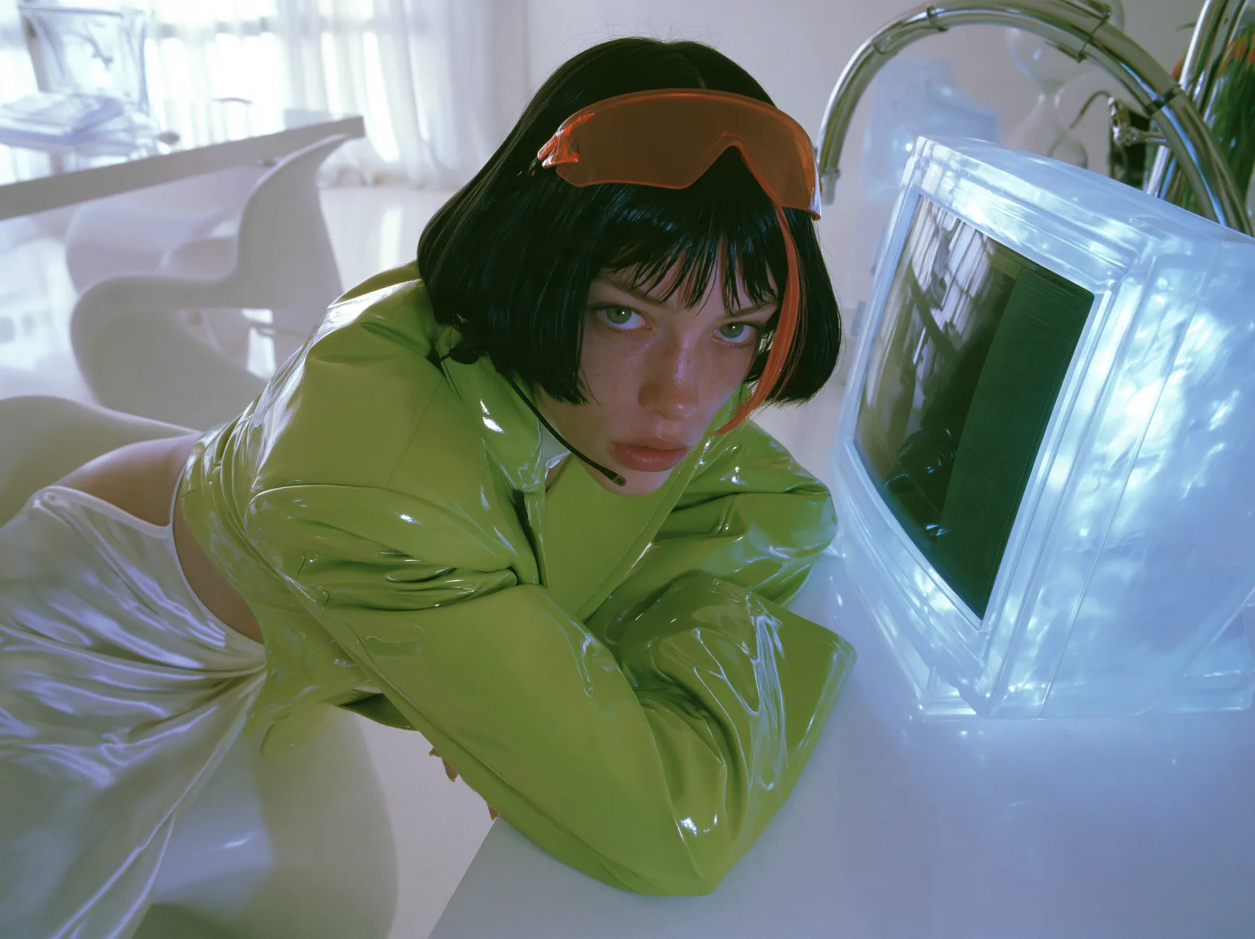 Y2K high fashion editorial, a 2001 couture magazine story: a young Caucasian American woman with pale skin and a glossy black blunt bob with heavy straight bangs and one clay-orange streak, a thin black headset…